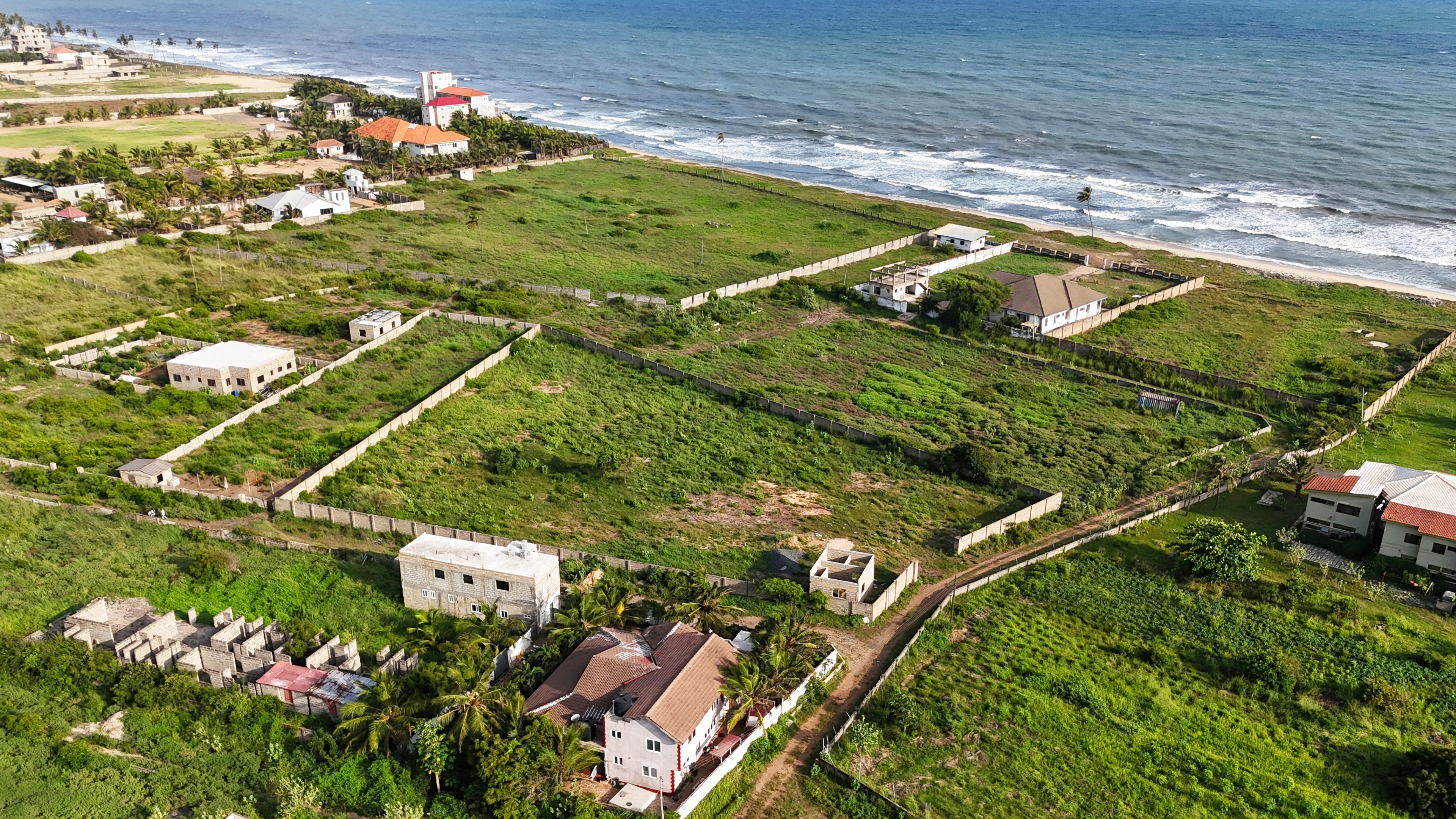 Aerial view of undeveloped coastal residential lots with palms, nearby homes, and ocean frontage